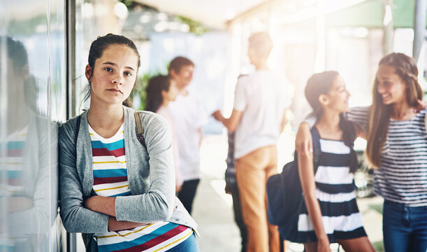 Young girl, portrait and lonely with school bag outside classroom in learning academy or institute. Female person, teenager or learner leaning on glass wall alone with arms crossed at outdoor campus
