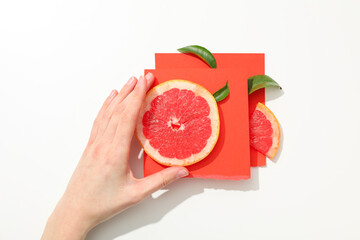 Slices of grapefruit on orange paper pieces and female hand on white background, top view