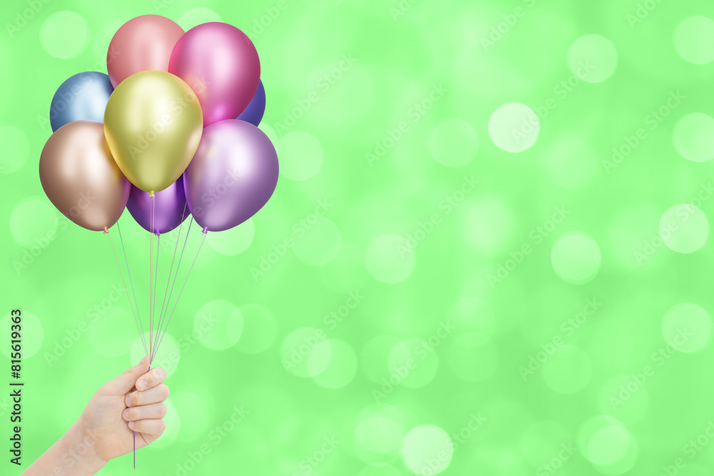 Poster childrens hand holds bunch of colorful shiny balloons on blurred summer green background. empty spac
