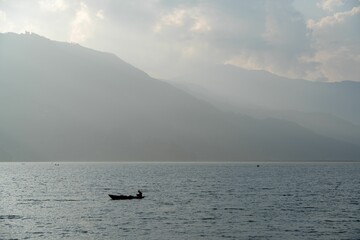 Obraz premium Small boat sailing in the middle of a vast lake surrounded by majestic mountains.