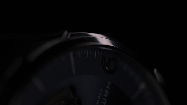 Closeup footage of the case body and crown of a black watch rotating on blur dark background