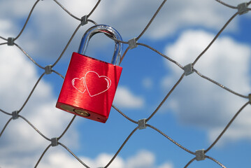 a single red love lock with two hearts hangs on a bridge railing