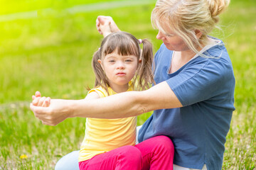 Happy family. Little girl with syndrome down and her mother play together in a summer park