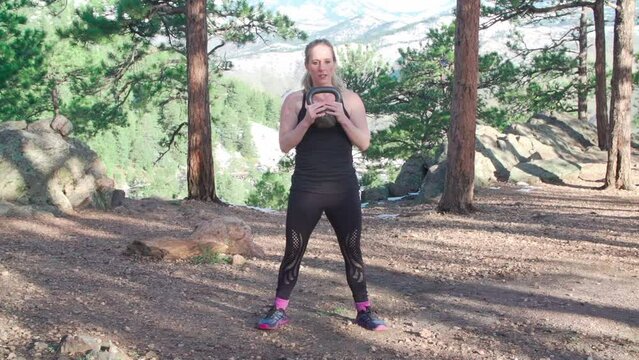 Caucasian fitness trainer doing the kettlebell goblet squat exercise in the park on a sunny day