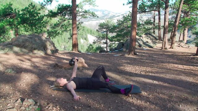 Caucasian fitness trainer doing the kettlebell Turkish get up exercise in the park on a sunny day