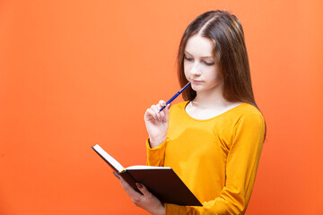 Winsome Blond Girl in Yellow Shirt Posing on Orange Background Studio Portrait as People Lifestyle Concept While Writing Notes in Notebook.