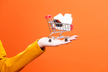 Healthcare Concepts. Female Woman Hand Holding Mockup Small Tiny Shopping Cart Trolley With Bunch of Medicines Against Trendy Orange Background.