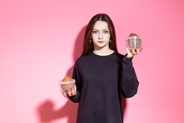 One Winsome Smiling Teenager Girl in Black Shirt Posing with Coconuts Placed in Plastic Containers On hands Indoors Against Pink.