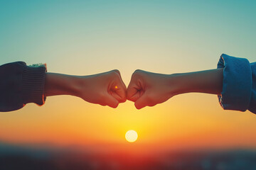 Hands of friends giving fist bump to each other against clear sky during sunset