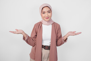 Smiling young Asian Muslim woman wearing hijab presenting copy space on her right and left side over isolated white background.