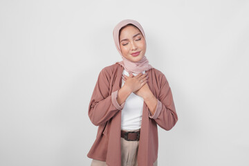 Happy mindful thankful young Asian Muslim woman wearing hijab hands on chest smiling isolated on...