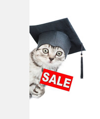 Cute graduated cat looks from behind empty white banner and  holds signboard with labeled "sale". isolated on white background