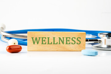 Wellness sign on a wooden bar in front of a stethoscope next to pills, vitamins