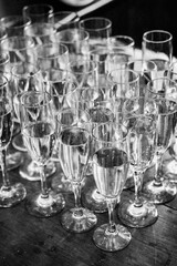 Group of glasses atop a wooden tabletop, illuminated by natural light from a window, in grayscale