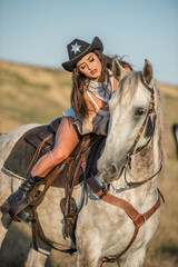Obraz premium Sexy cowgirl with hat on horseback in the desert. Beautiful girl in a cowboy hat on a horse. Beautiful cowgirl on horseback in the mountains. Outdoor lifestyle portrait