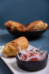 Top view of a crispy potato with a meat filling inside, accompanied by an onion and tomato salad.
