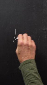 Hand writes the number 5 with white chalk on a black board. Vertical video