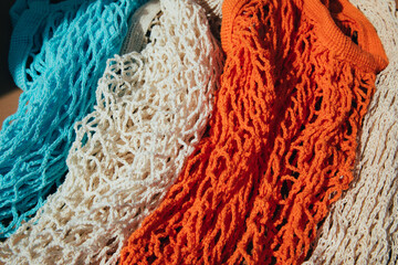 Reusable mesh bags in blue, orange and beige on a brown background in sunny daylight. Mesh shopping bags. Sustainable use concept