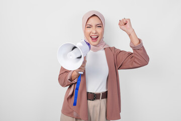 Young Asian Muslim woman wearing hijab shouting at megaphone with happy successful expression and...