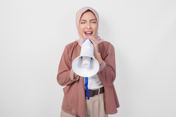 Lively young Asian muslim woman wearing hijab shouting at megaphone, isolated on white background.