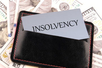 Debt relief concept. A word INSOLVENCY on a business card in a leather accessory on the background of banknotes