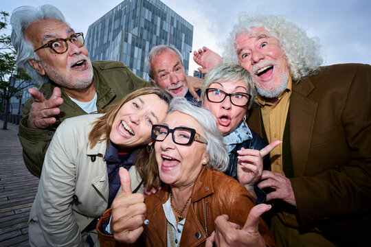 Funny flash portrait of group seniors Caucasian people posing making gestures together outdoors. Older friends with gray hair looking joyful at camera dusk in city. Lifestyle happy matures partners