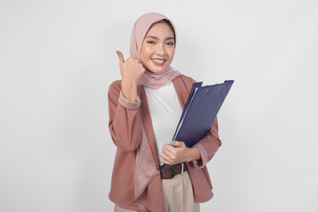 Smiling Asian woman wearing hijab holding document and giving thumbs up hand gesture of approval on...