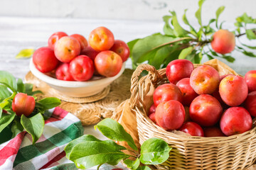 Red fresh ripe plums with water drops in wicker container on white wooden table, organic plums served for eating, healthy food and fruit concept