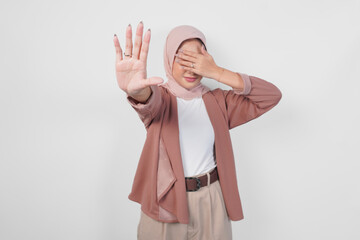 Beautiful Asian Muslim woman wearing a hijab with hand gesture posing rejection or prohibition,...