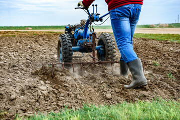 Man cultivating soil with tiller block in spring.