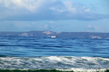 Small sailing boat is pictured in the open ocean, with a stunning mountainous landscape