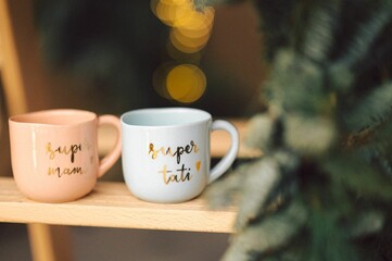 Rustic wooden table with two ceramic coffee cups sitting in front of a Christmas tree