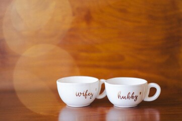 Pair of porcelain mugs arranged on top of a wooden table against Christmas bokeh lights