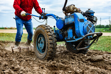 Man cultivating soil with tiller block in spring.