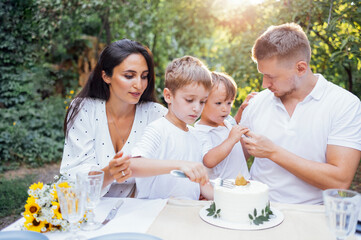 Mom, dad and two little sons in white clothes eat cake in an open air cafe