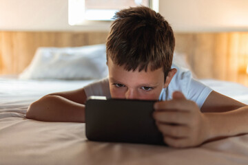 Cute little boy lying on his bed at home using a smart phone.