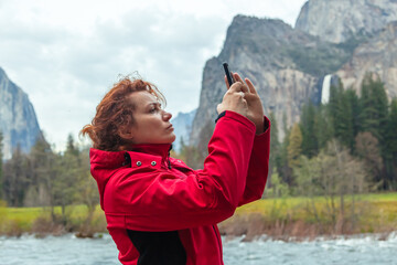 Young woman takes pictures of a natural landscape in Yosemite Park, California with a smartphone...