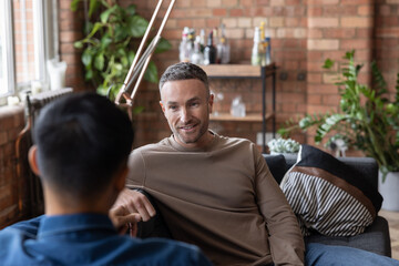 Two mid adult males at home sitting on a sofa talking 
