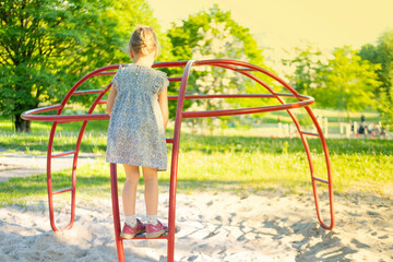 little girl in blue short dress walks on playground equipment, joyful childhood, outdoor fun in rays light, happy childhood, , vestibular apparatus training