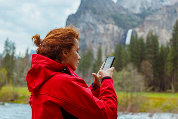 Woman in a red jacket takes photographs of nature in the American Nature Park. USA, California,...