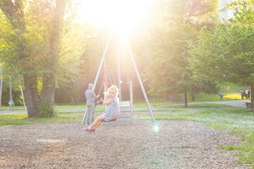 happy preschool girl swings high on summer day, blurred child figure in rays light, joyful Carefree...