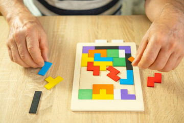 male hand manipulates colorful wooden puzzle, elderly old man composing geometric shapes, brain...