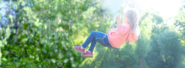joyful little girl ascends into sunny sky on swing, blurred child figure in rays light, happy...