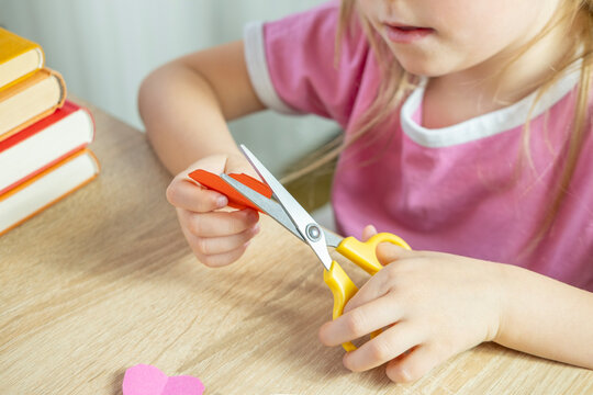 left-handed little girl learning to cut paper with scissors, making shapes like a house, heart and flowers for applique crafts
