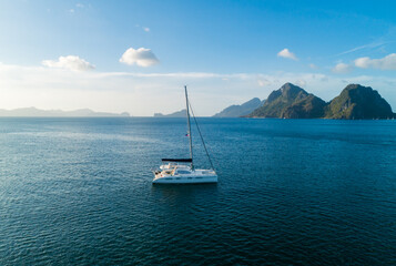 Fototapeta premium Sailboat anchored in pristine tropical waters near scenic islands at sunset