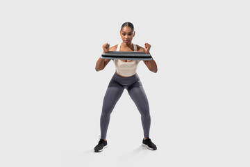 A focused African American woman is engaging in a fitness routine using a resistance band to...