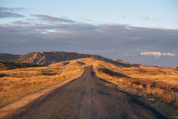 Sunrise on an empty country road passing through amazing hilly landscape. Colorful grassy and hilly...