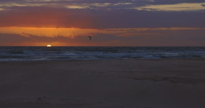 Kitesurfer kiting with kite and board in the ocean with calm waves at sunset with sun in the background