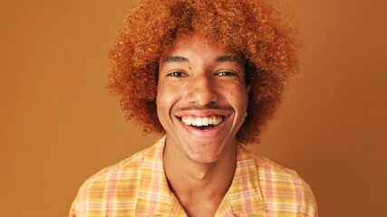Close up, portrait of a stylish curly guy smiling broadly looking at the camera isolated on brown...