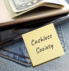 Yellow note on jean mobile and cash dollar money, with text written CASHLESS SOCIETY, when paying...